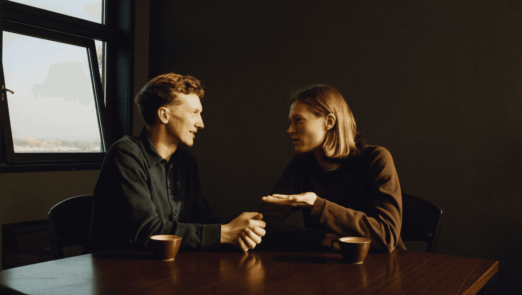 Two people talking at a table, one showing something with an open hand.