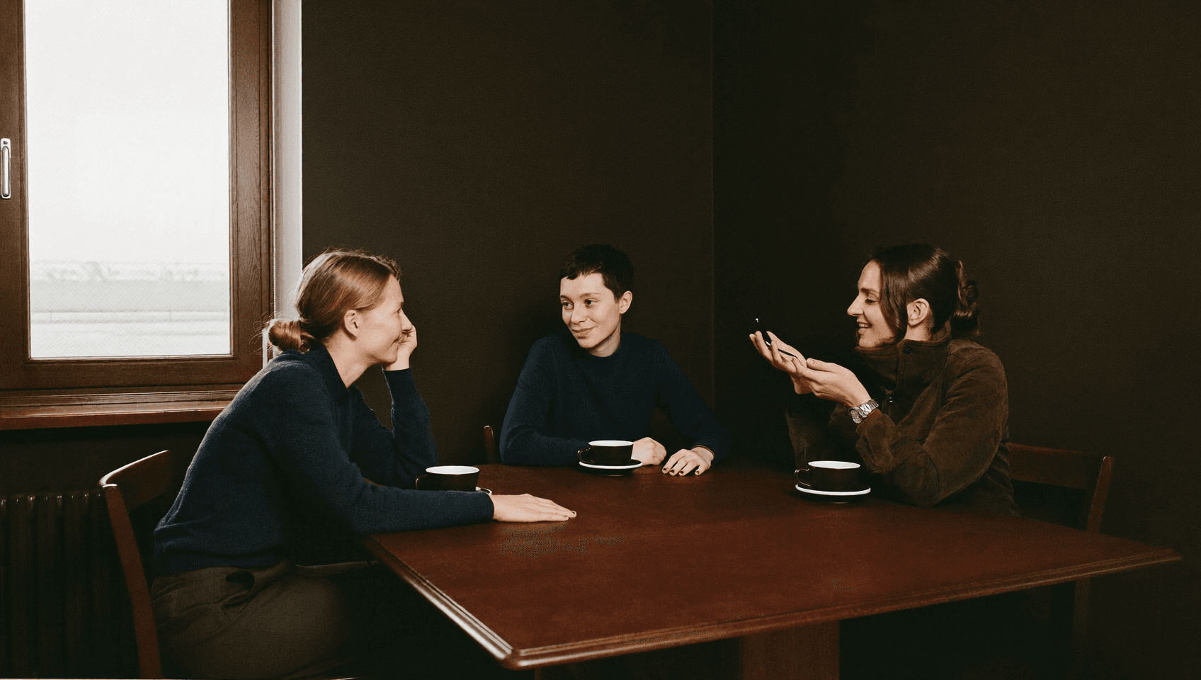 Three people at a long table, one talking and the others listening with a smile.