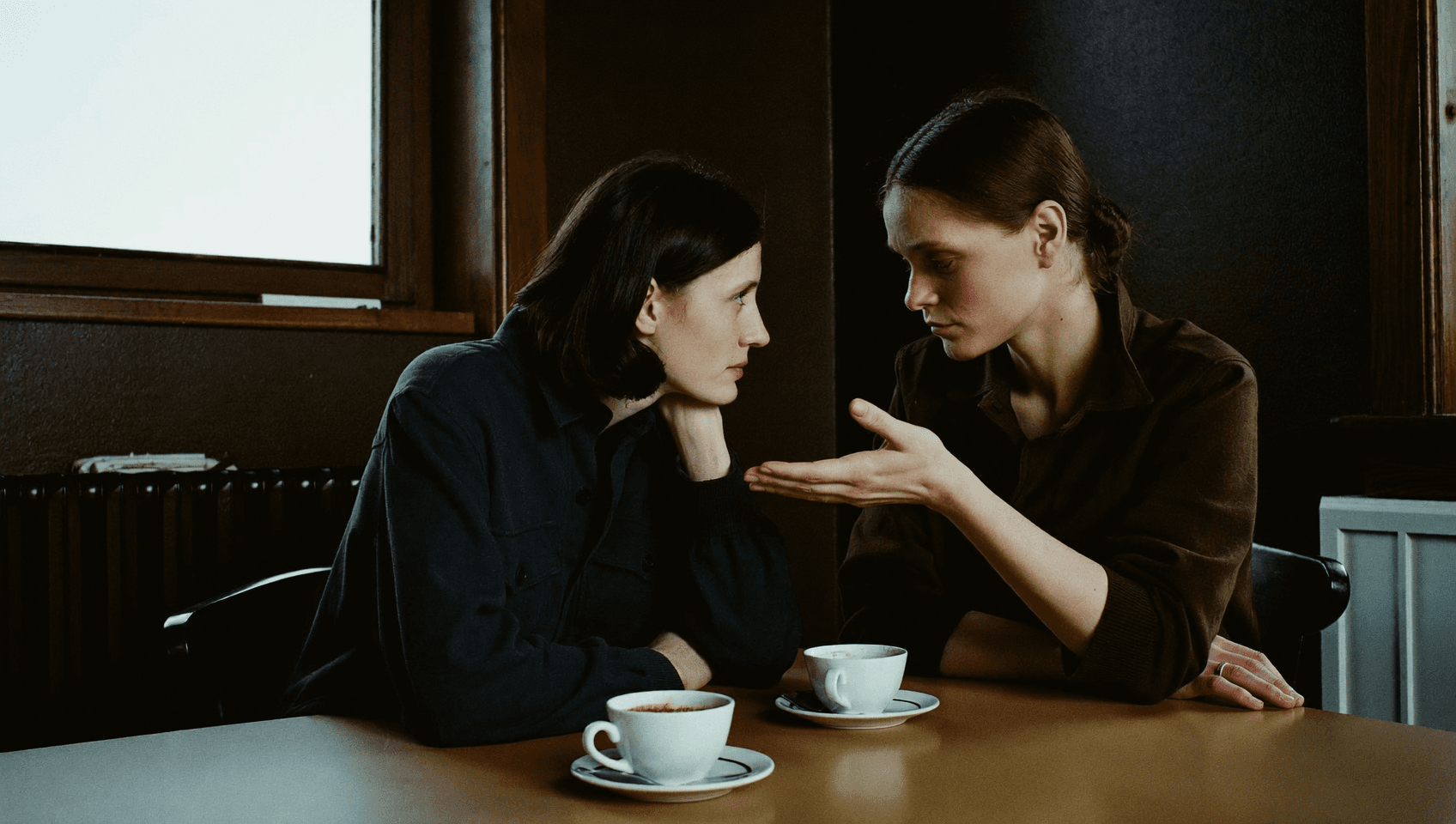 Two people leaning towards each other over a table, cups standing beside them.
