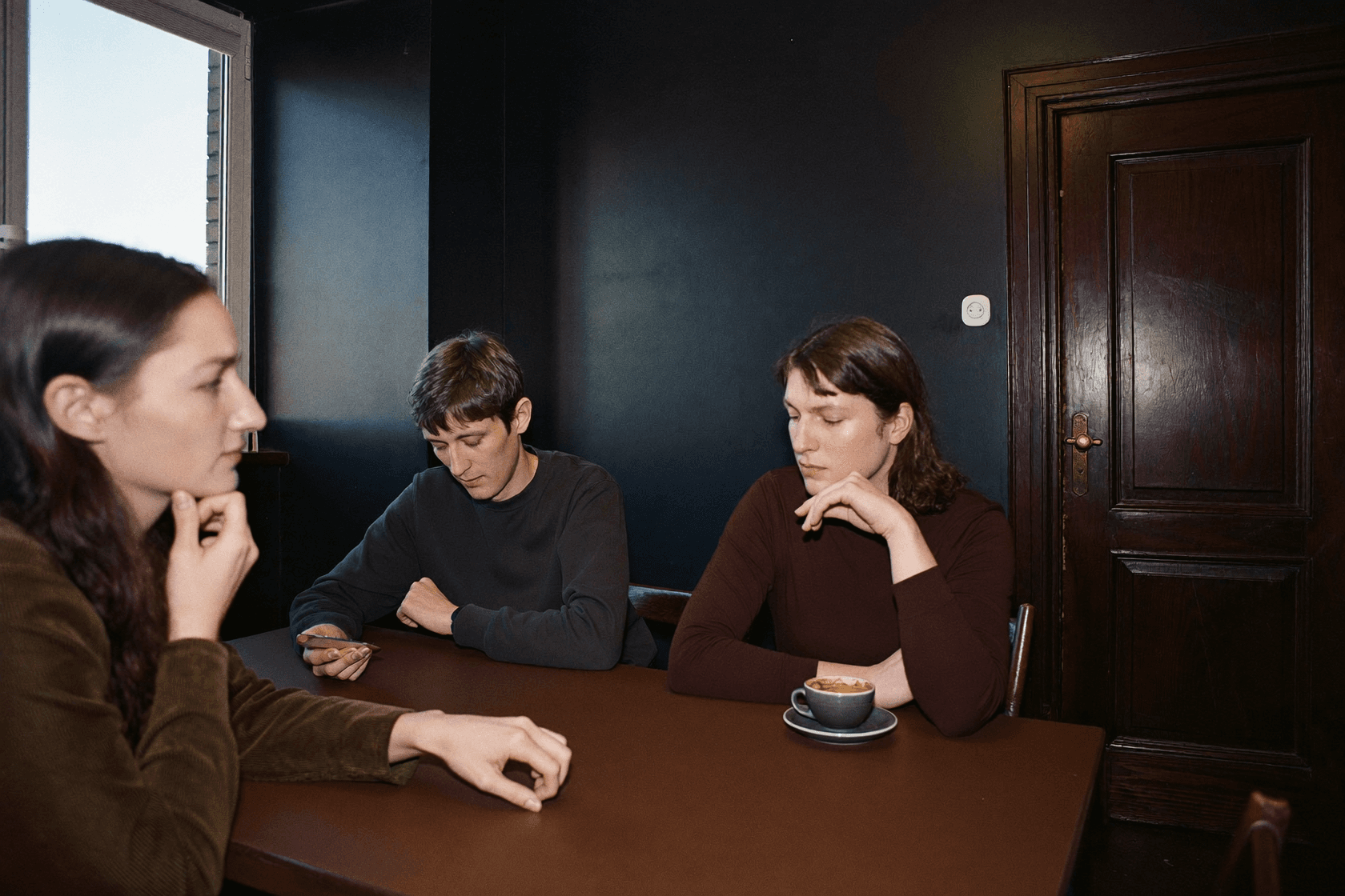 A person at a table propping up their face with one hand and looking aside, the rest of the group beside them.