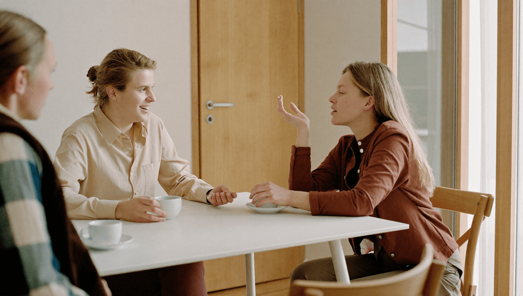 Two people at a table, one speaking with a raised hand while the other listens.