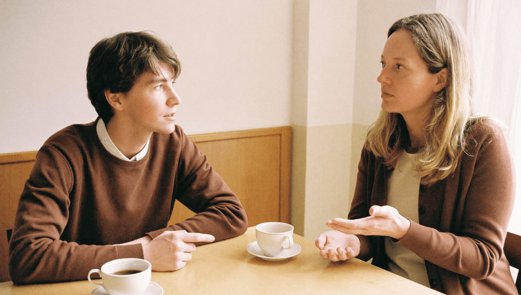 Two people talking at a table, one showing something with an open hand.