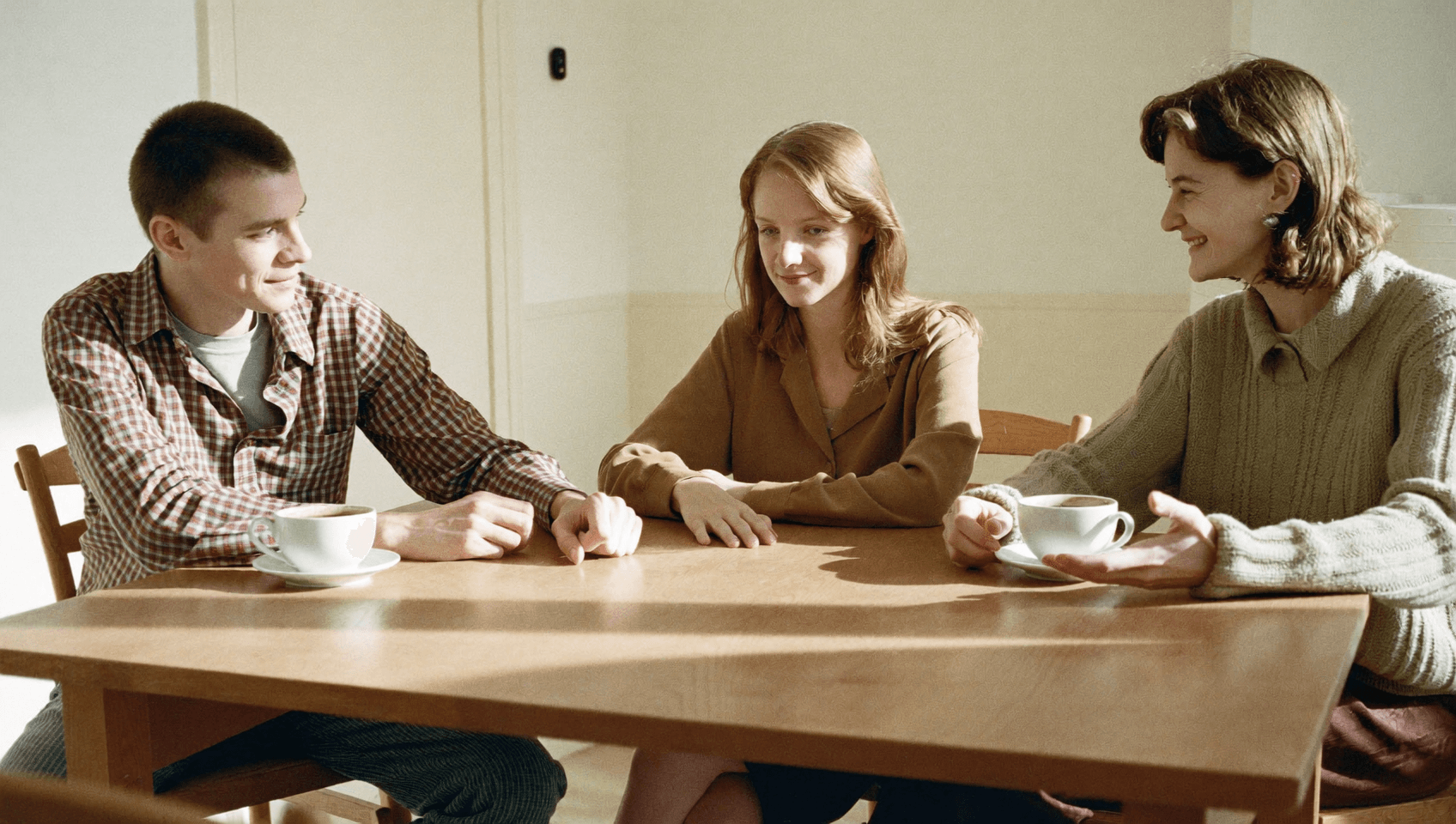 Three people at a long table, one talking and the others listening with a smile.