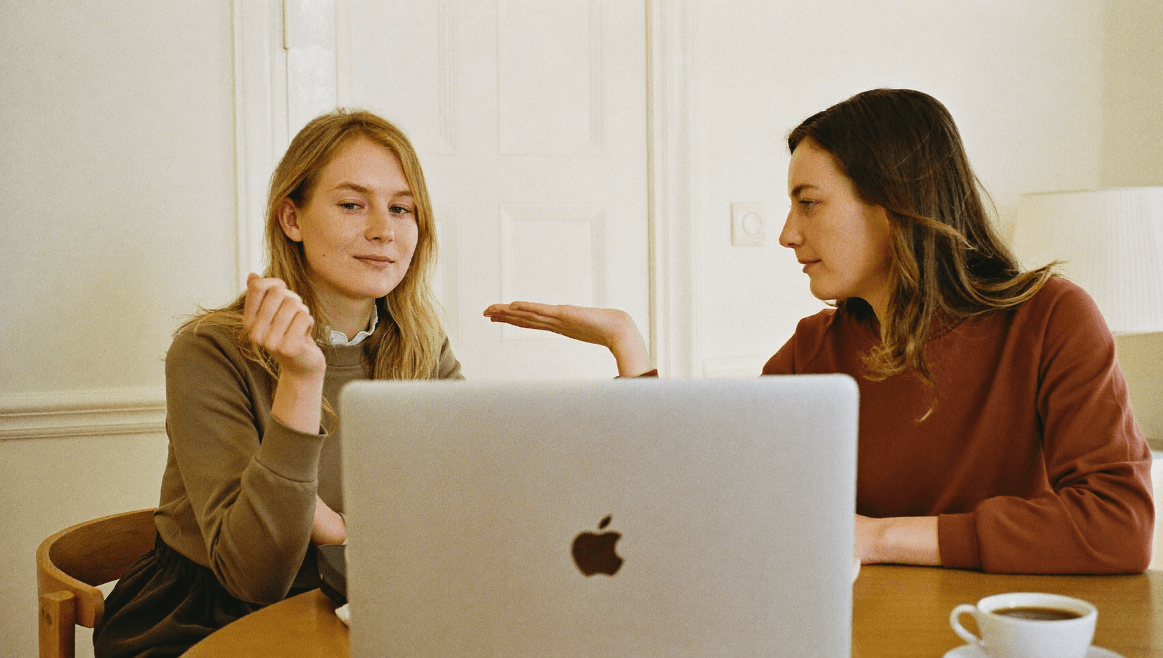 Two people talking over an open laptop, seen from behind the lid.