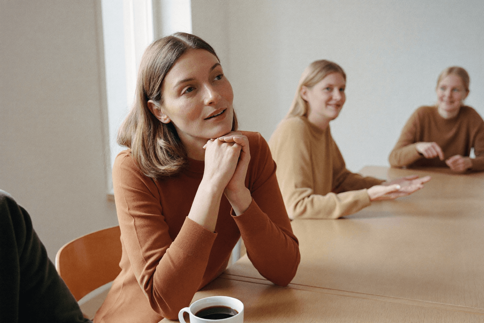 Several people at a table, the one in the middle of the frame looking at the others, a cup in front of them.