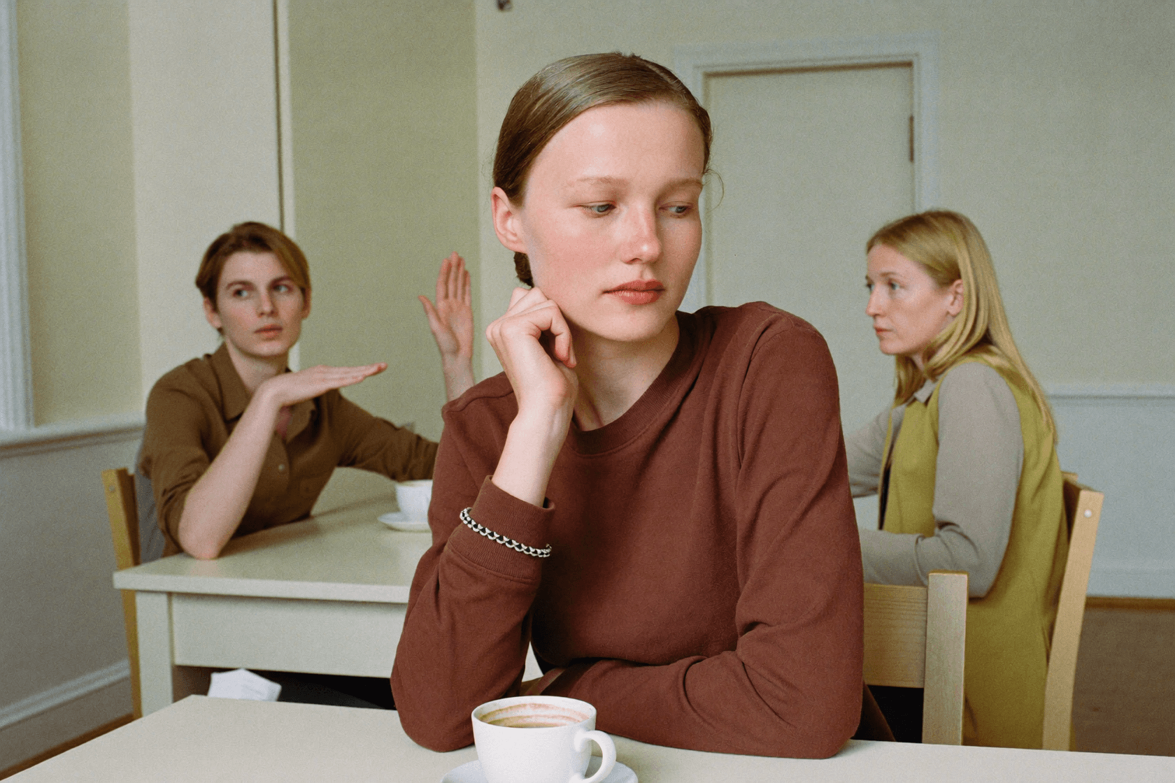 A person at a table propping up their face with one hand and looking aside, the rest of the group beside them.