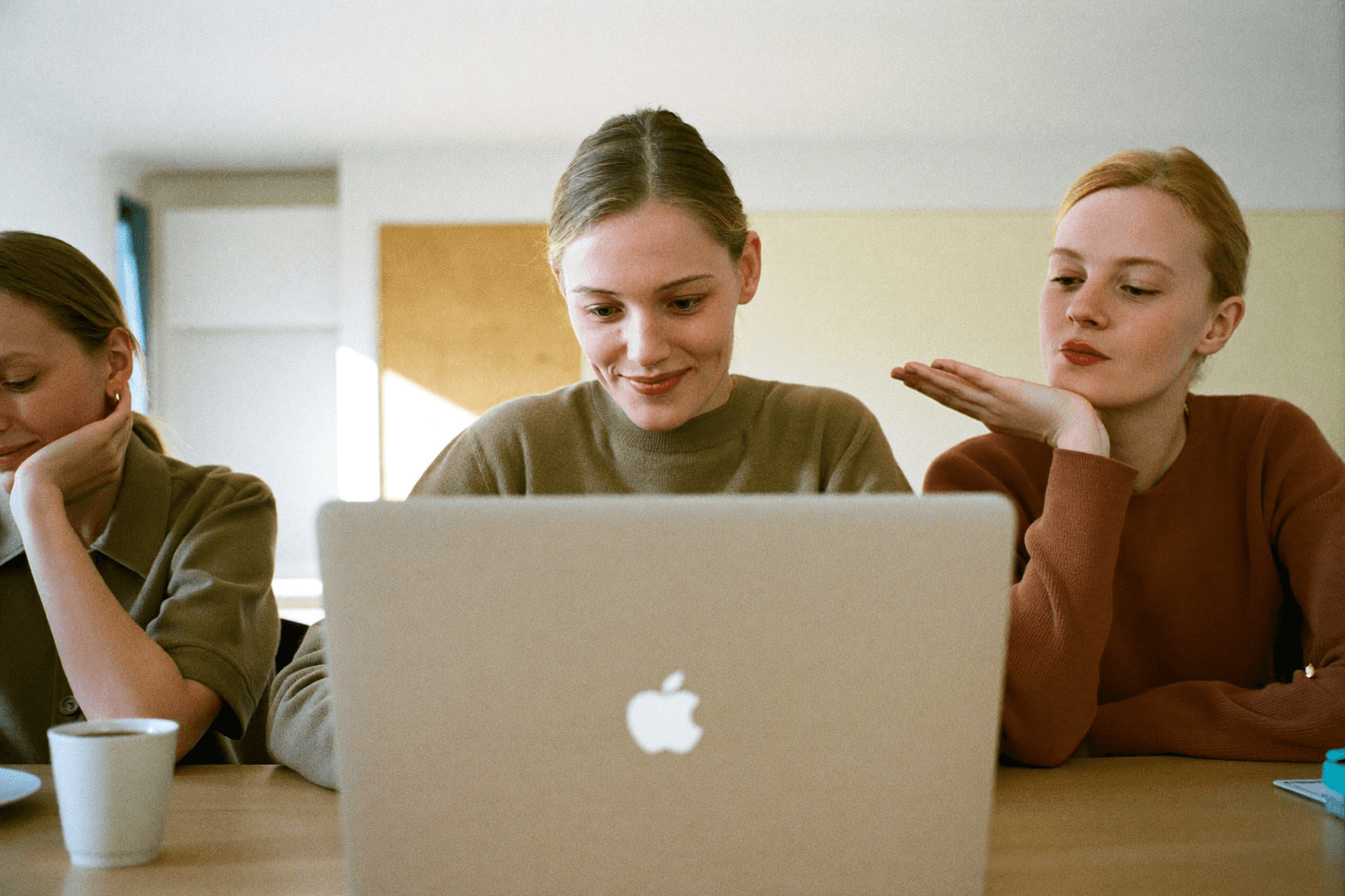 An open laptop in the foreground, someone looking at the screen behind it and a raised hand beside them.